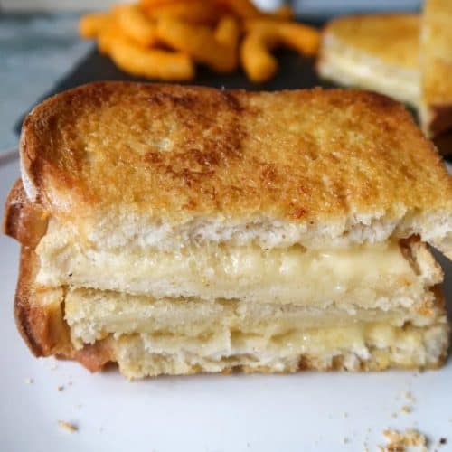 two halves of grilled cheese stacked on top of each other with insides showing on a white plate