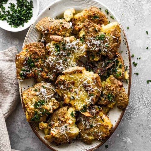 overhead of garlic Parmesan smashed potatoes on serving dish with parsley garnish