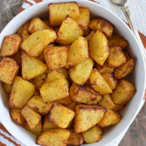 overhead of home fries in white bowl with fork to the right