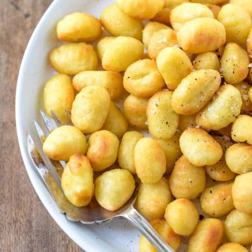 overhead of gnocchi in white serving dish garnished with salt and pepper with serving fork