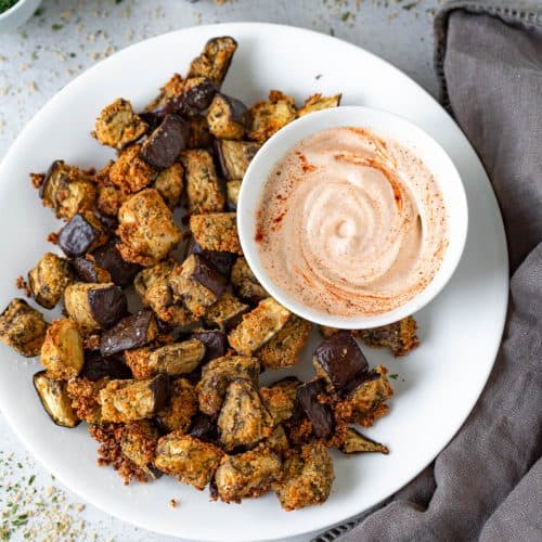 overhead of eggplant bites on white plate with side of dipping sauce