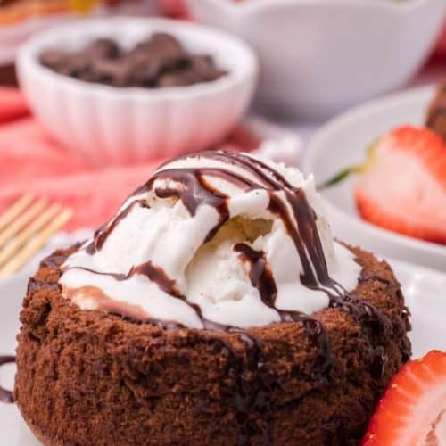 lava cake topped with ice cream and syrup with a cut strawberry on the side