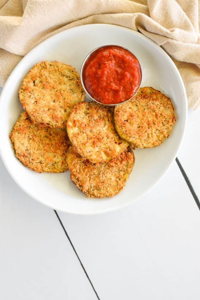 overhead of eggplant slices on a white plate with a side of sauce in a small cup