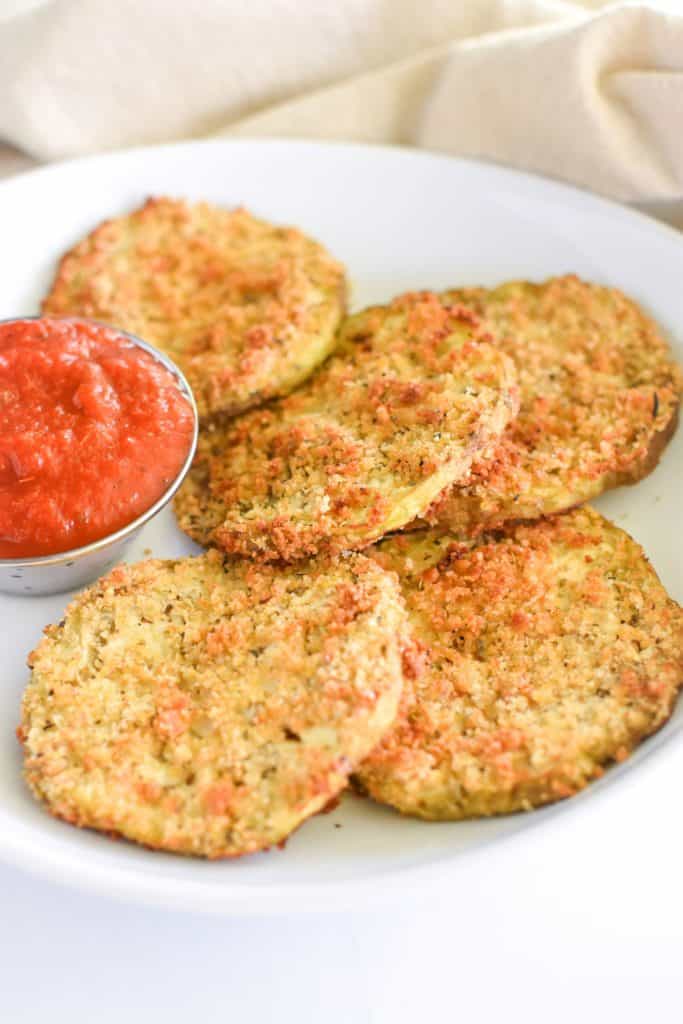 front view of eggplant slices on white plate with cup of sauce partially cut of on the left