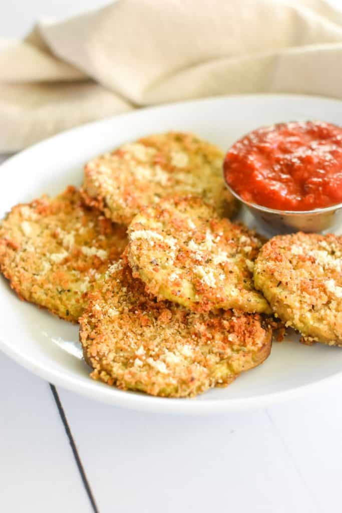 front view of eggplant slices garnished with vegan Parmesan on a white plate with a cup of sauce