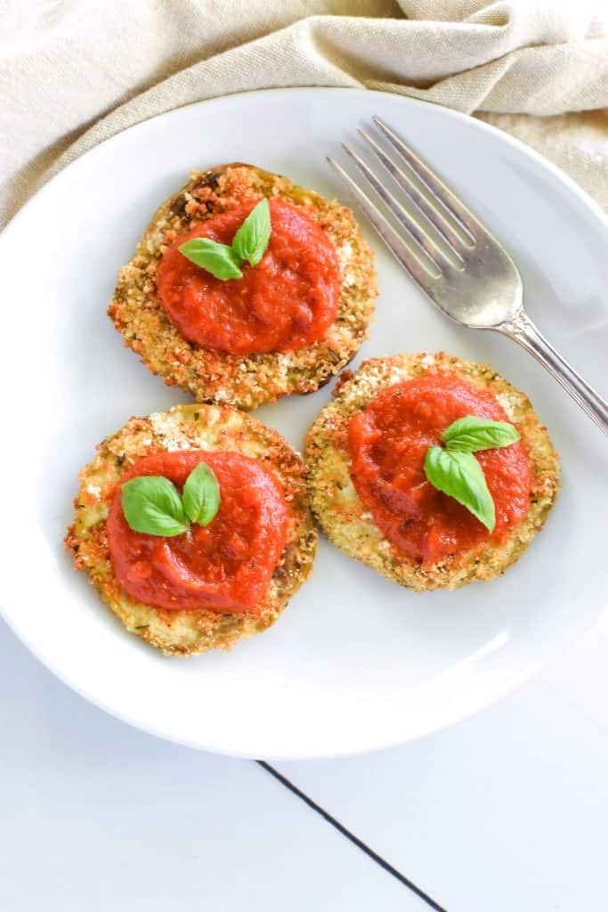 overhead of eggplant slices topped with tomato sauce and garnished with basil with a fork on the plate