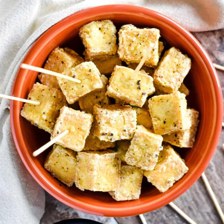 overhead of tofu in a bowl with toothpicks in some of the pieces.