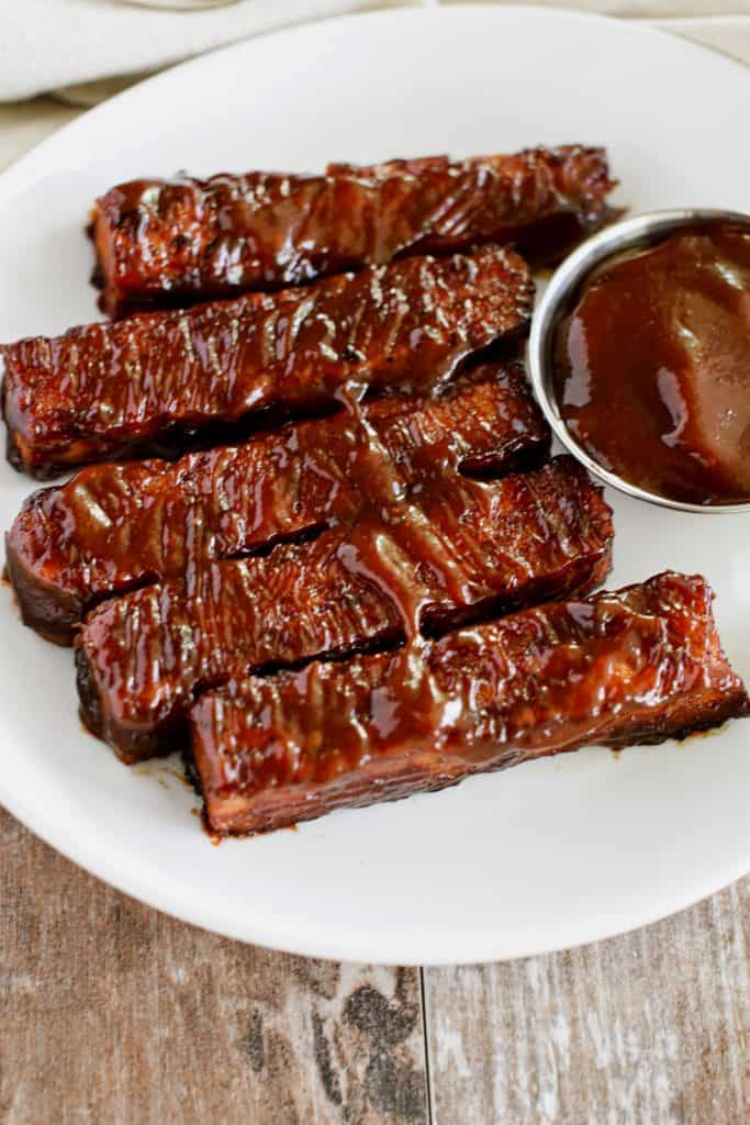 5 tempeh strips on a white plate with a cup of BBQ sauce.