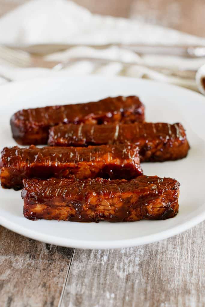 front view of tempeh strips on a white plate.