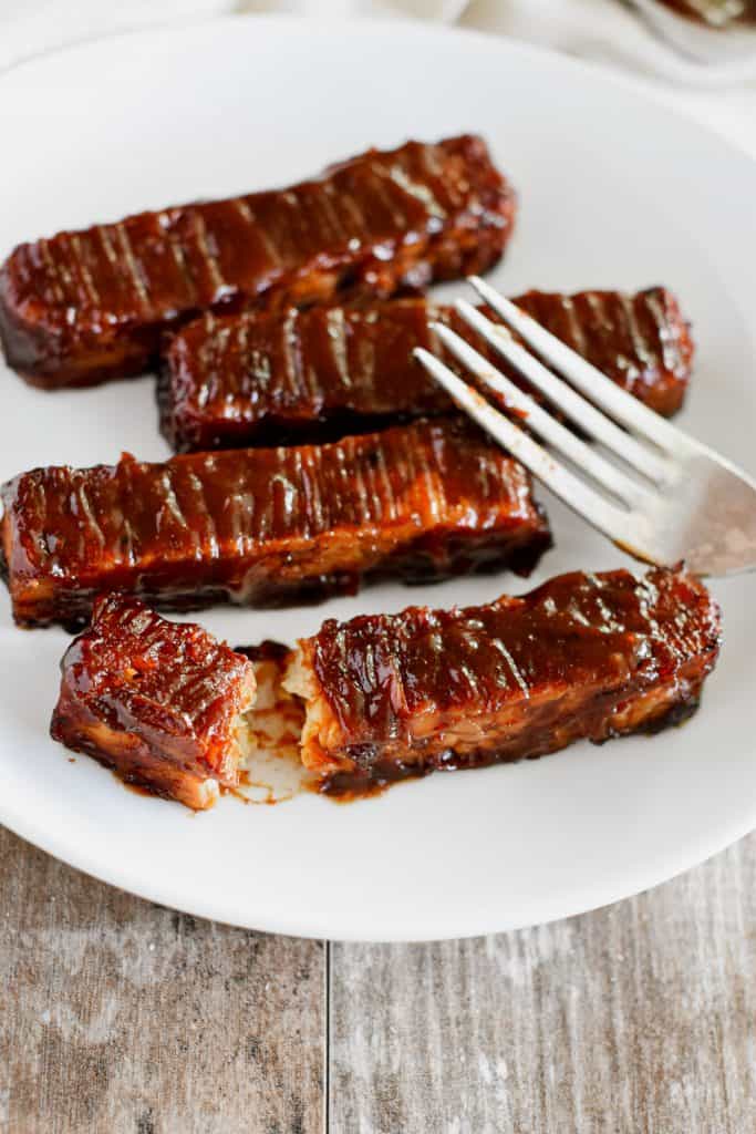 cut open tempeh strip with fork on a plate with more tempeh strips.