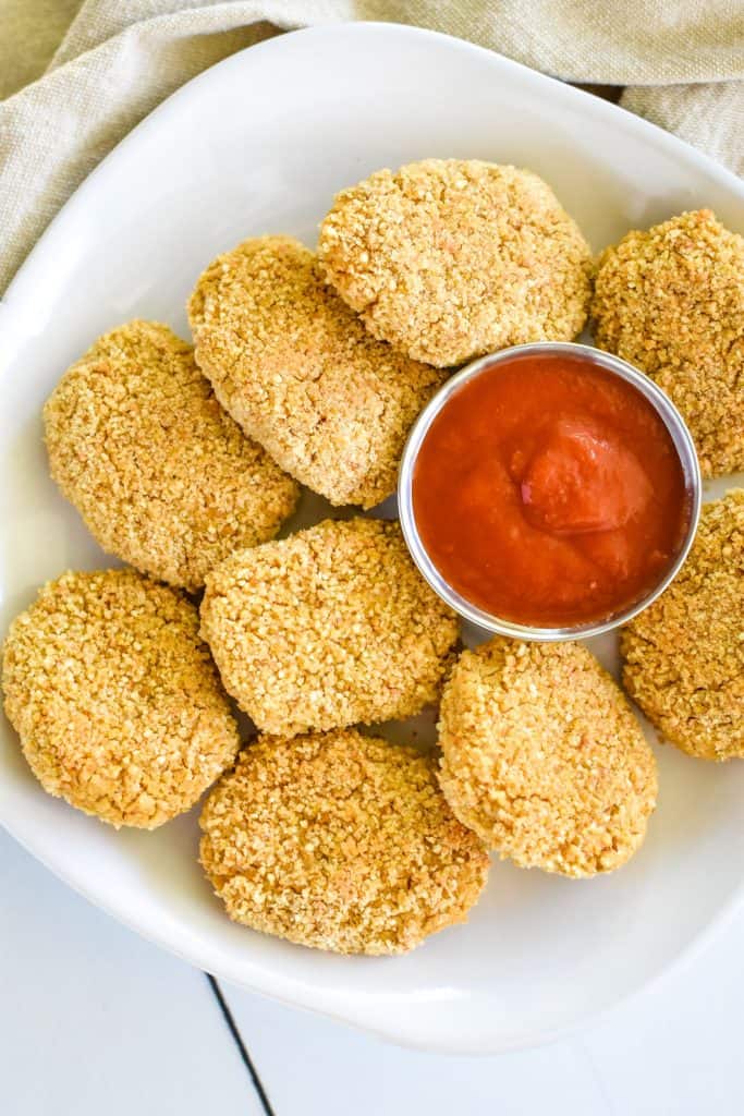 close-up overhead of chickpea nuggets on a white plate with small cup of ketchup off center and part of right side of plate cut off