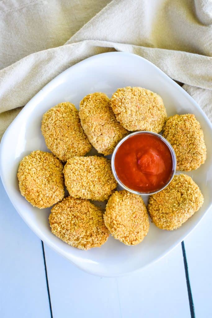 overhead of nuggets on a white plate with ketchup cup off center and kitchen napkin behind the plate