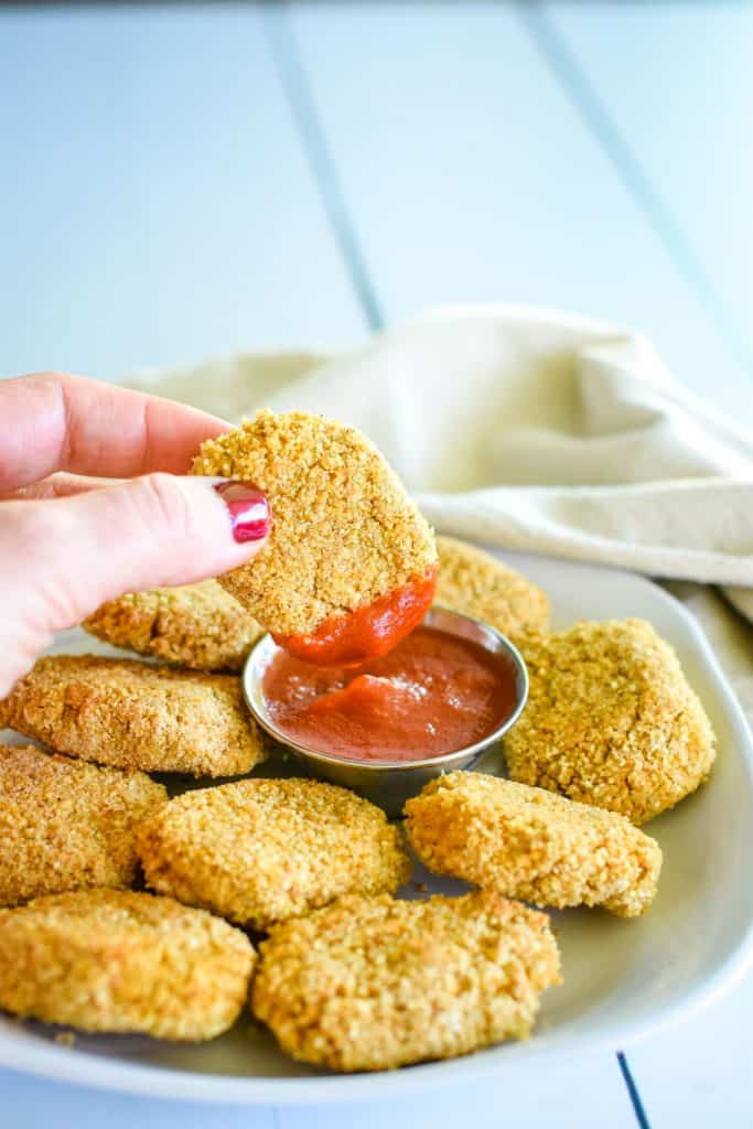 holding nugget that was just dipped in ketchup over the ketchup on a plate with more nuggets