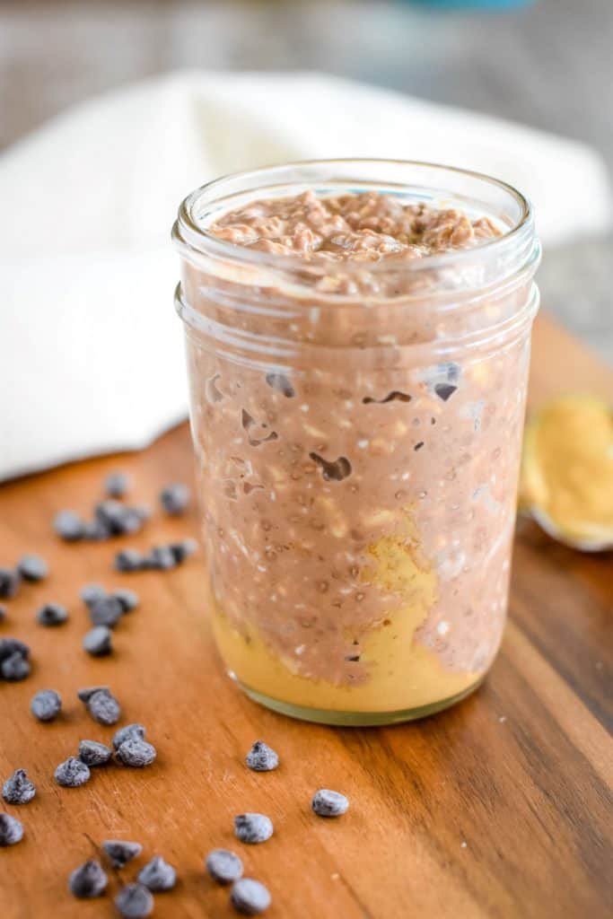 front view of oats in a mason jar on a wooden board with some chocolate chips around