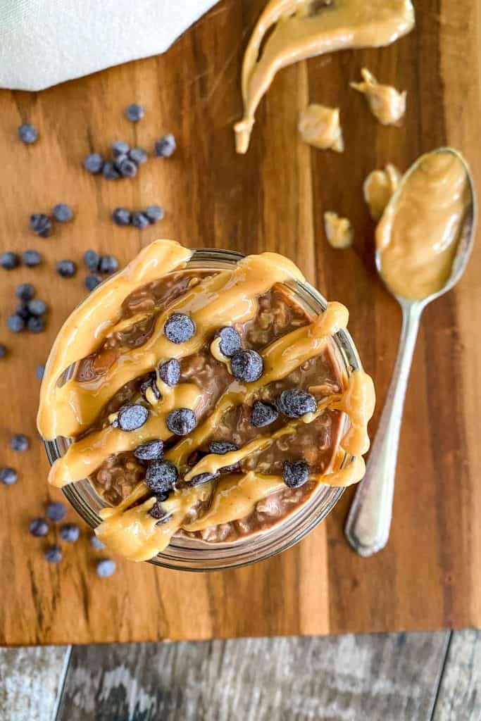 overhead looking into mason jar of overnight oats topped with extra peanut butter and chocolate chips and spoon of peanut butter on the side