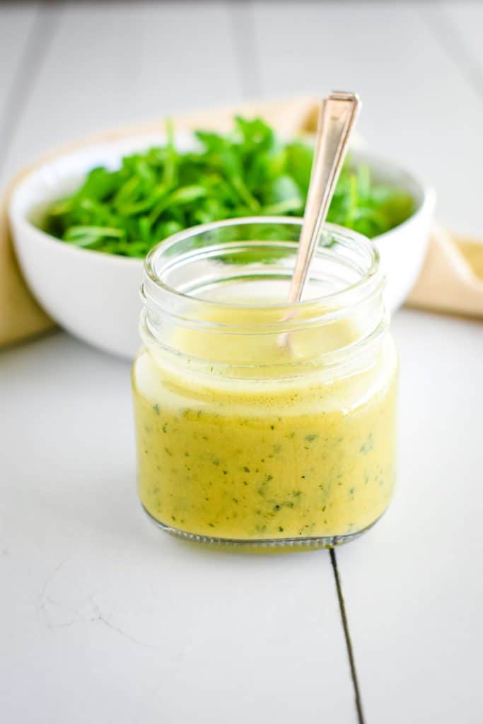 mason jar of dressing with bowl of greens behind it.