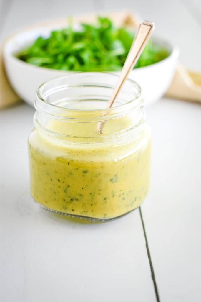 mason jar of dressing in front of bowl of greens.