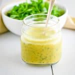 close-up of dressing in mason jar in front of bowl of greens.