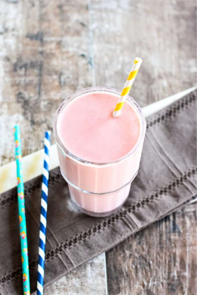 slight overhead of smoothie in a glass with straw in it and two straws on the side