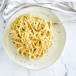 overhead of pasta on white plate with pepper and pumpkin Parmesan garnish and a fork twirling the pasta