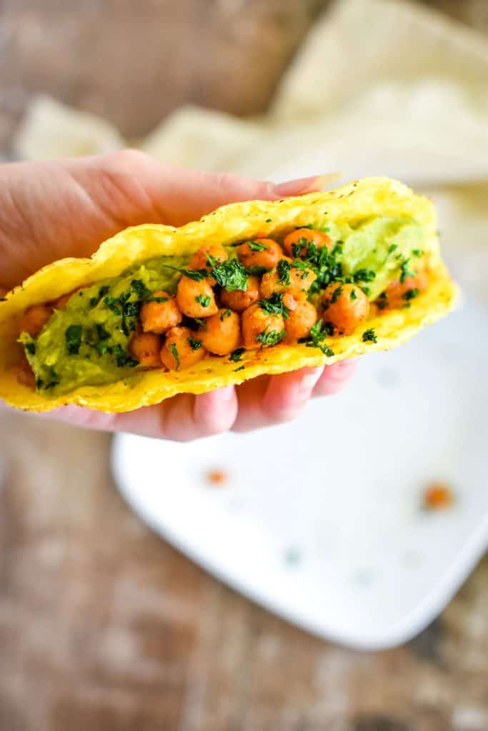 hand holding up a taco over a white plate below.