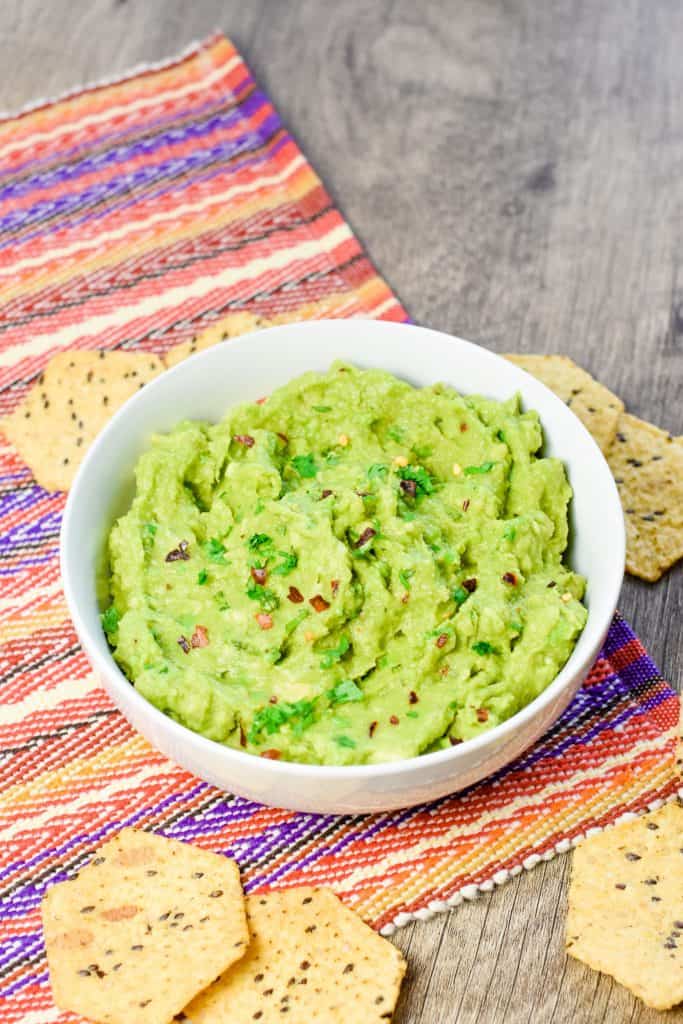 slight overhead of guacamole in white bowl with some chips around.