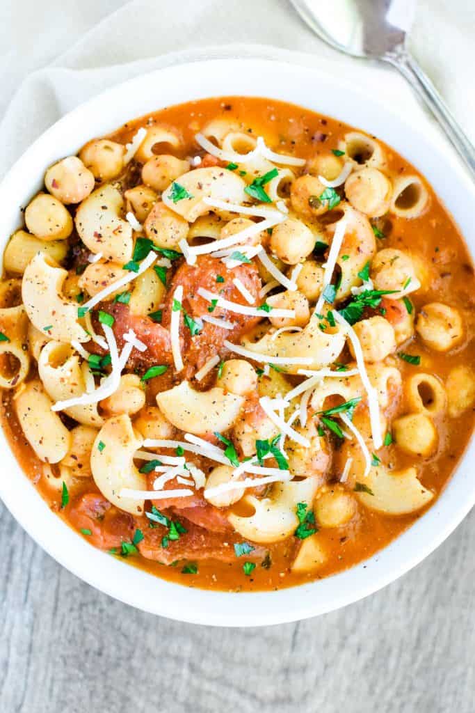 overhead of pasta e ceci in white bowl garnished with pepper, parsley and vegan Parmesan.