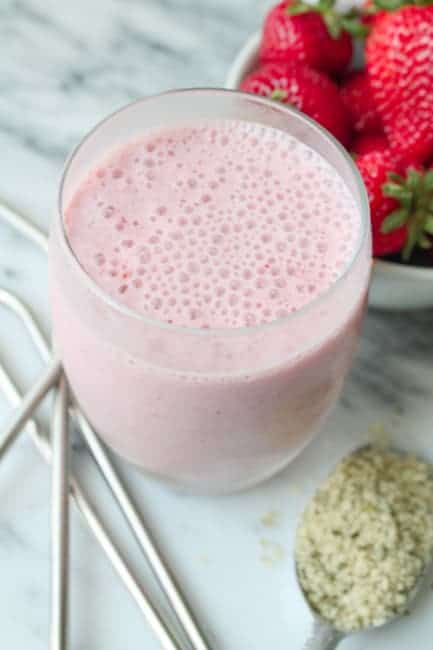 strawberry hemp milkshake in a glass with hemp seeds, straws, and strawberries around.