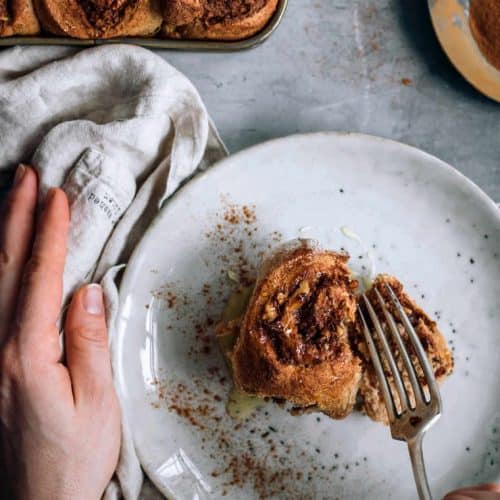 overhead of cinnamon roll on a plate with a fork cutting into it.