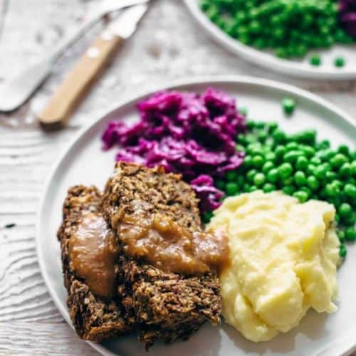 two slices of vegan meatloaf with gravy on plate with side dishes.