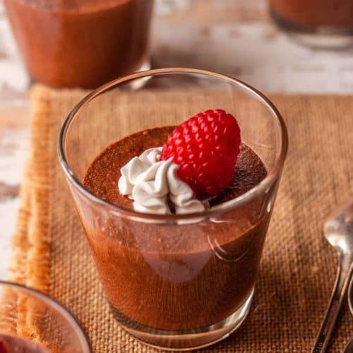 vegan chocolate mousse in glass with whipped topping and raspberry garnish.