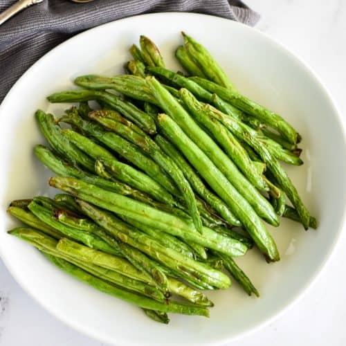 close-up overhead of green beans on a white plate.