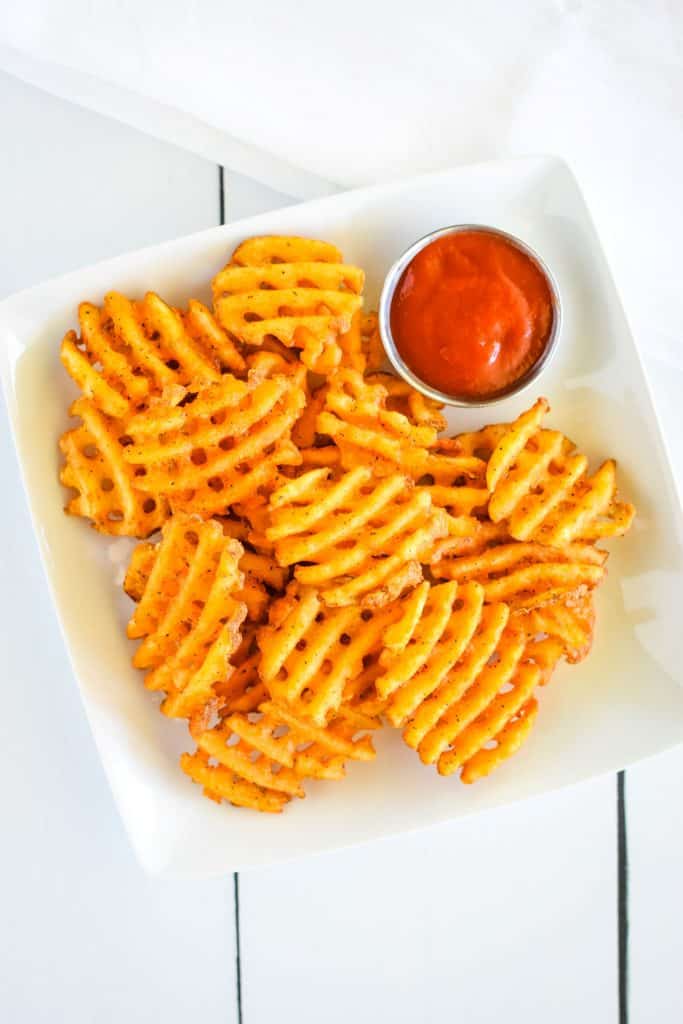 overhead of air fryer waffle fries on a white plate with ketchup and white napkin behind.