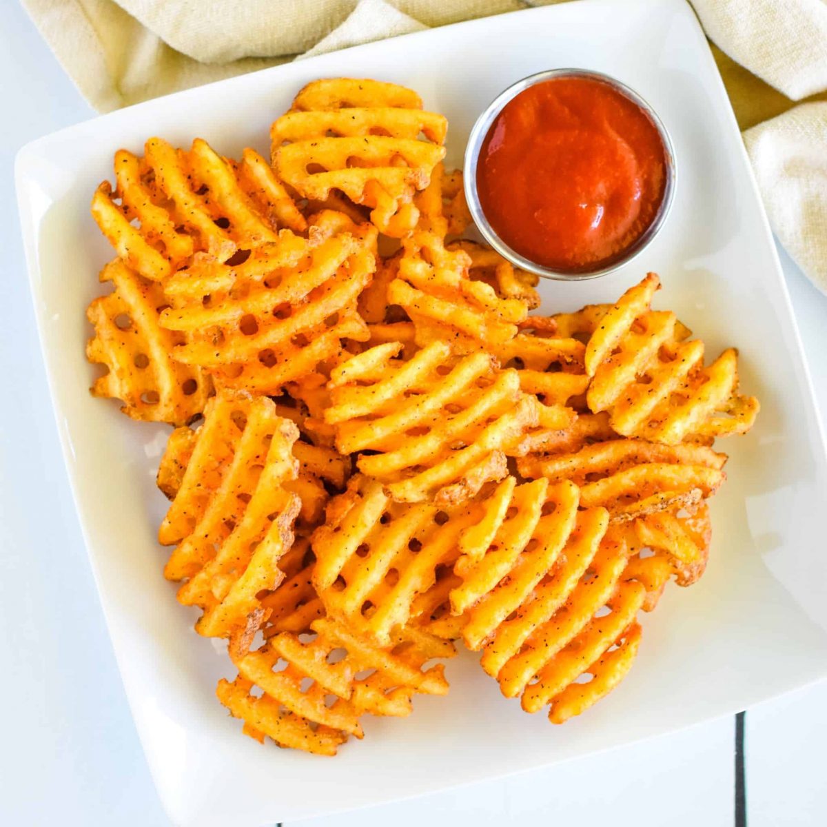 close-up overhead of waffle fries on a white plate with ketchup.