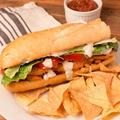 Buffalo soy curl sub on a white plate with tortilla chips.