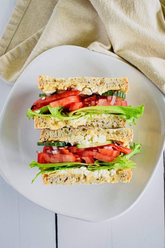 overhead of two halves of panera mediterranean veggie sandwich open on a white plate.