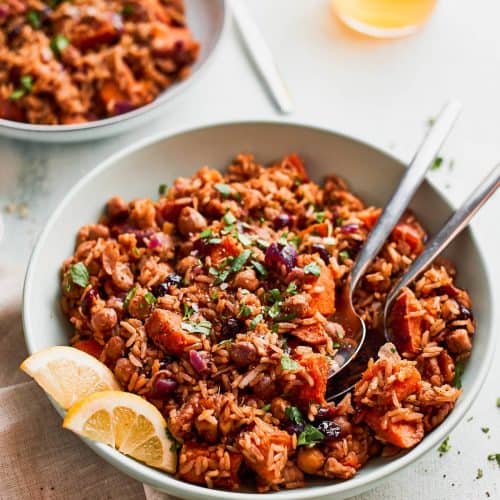 overhead of vegan pilaf with sweet potatoes in a white bowl with two spoons.