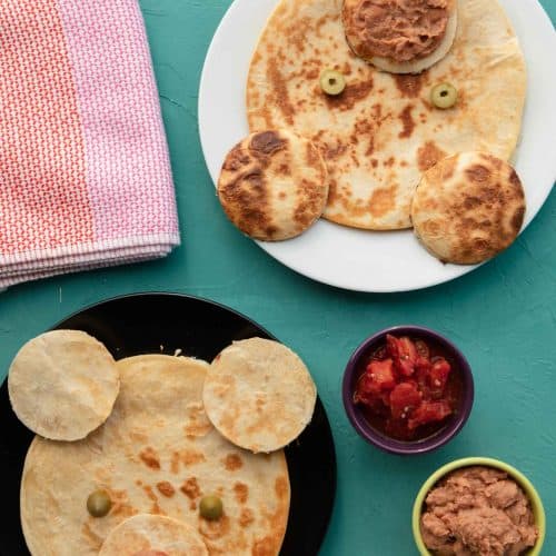 quesadillas made into bear faces on plates on a teal surface.