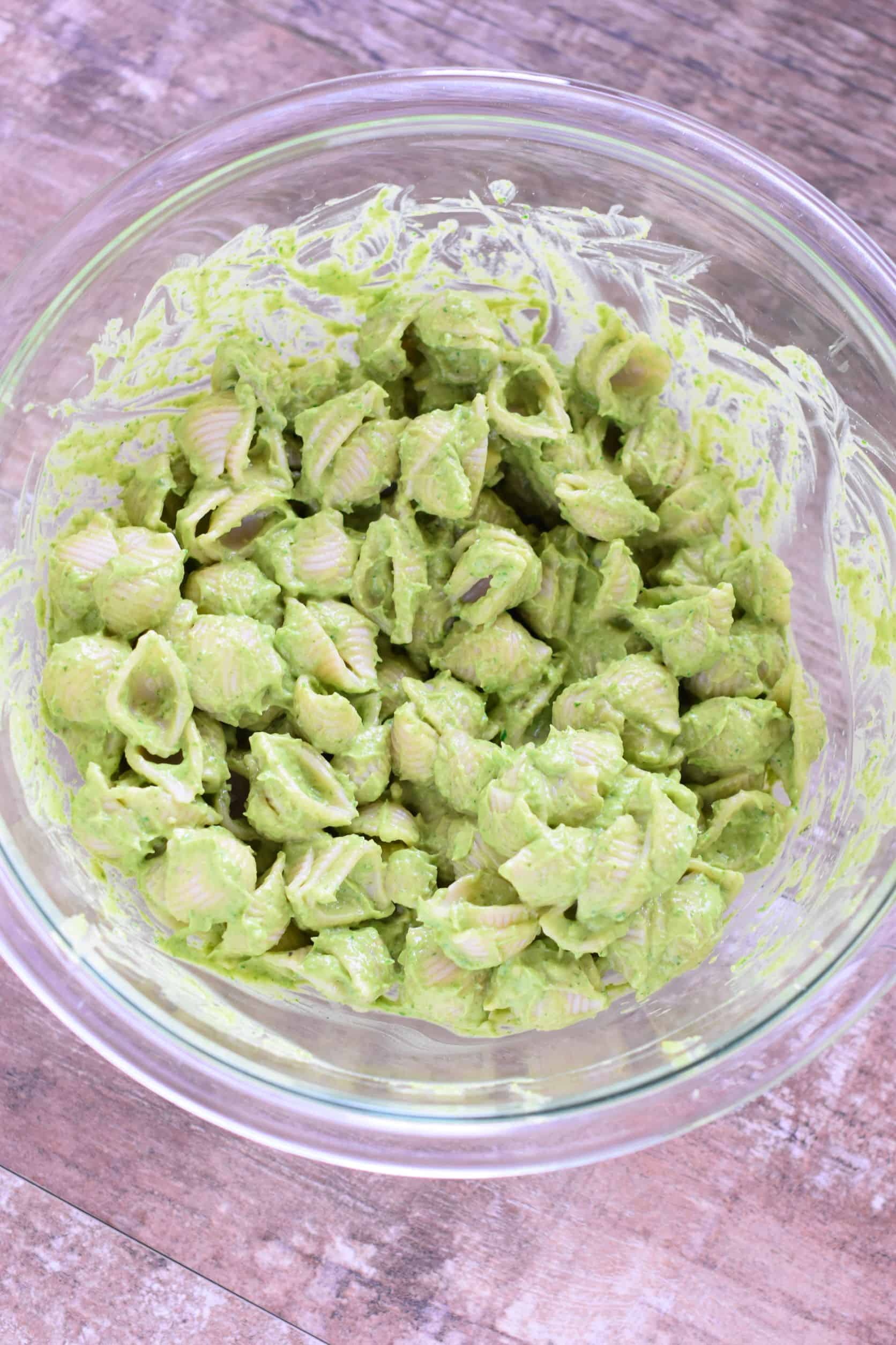 Pasta mixed with dressing in mixing bowl.