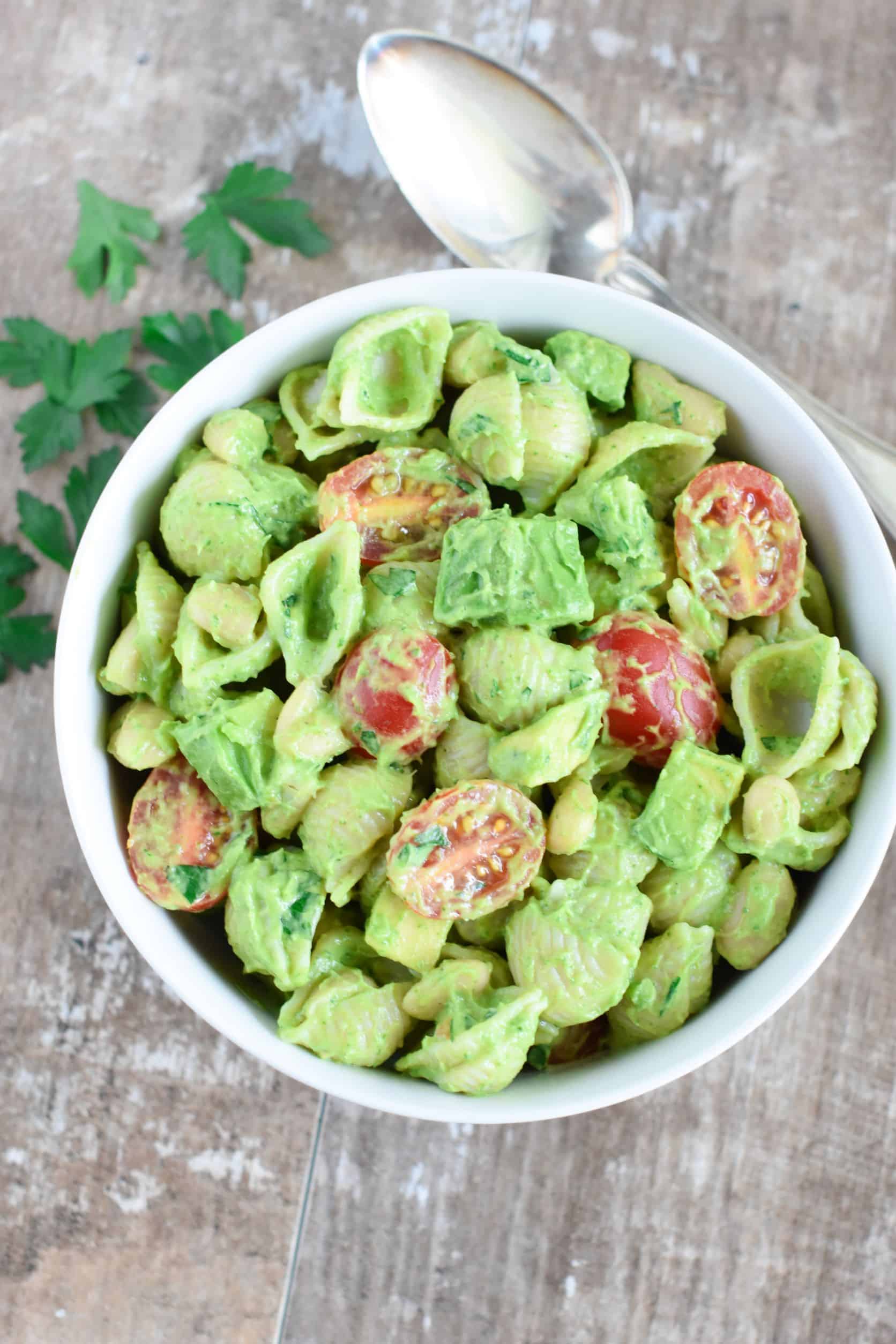 overhead of pasta salad in white bowl with spoon back right and cilantro on table.