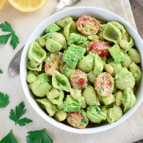 overhead of pasta salad in a white bowl with garnish around it.