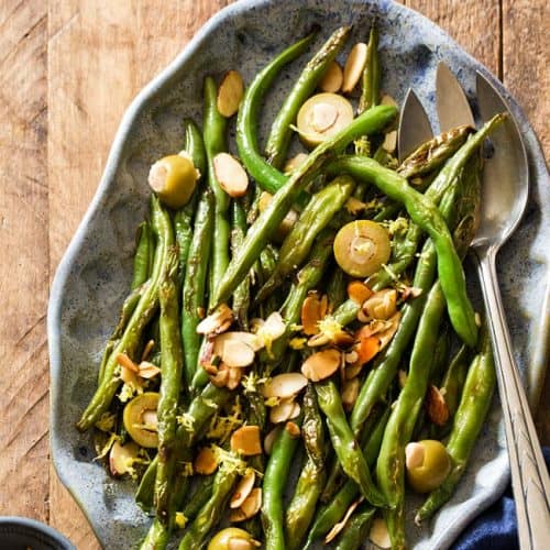 overhead of green beans with almonds and olives on a serving platter.