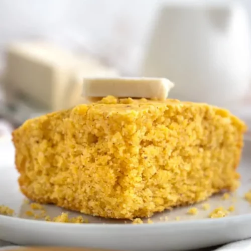 piece of cornbread on a white plate with pat of vegan butter on top.