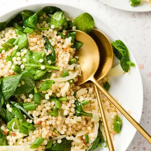 vegan couscous salad with two spoons in it.