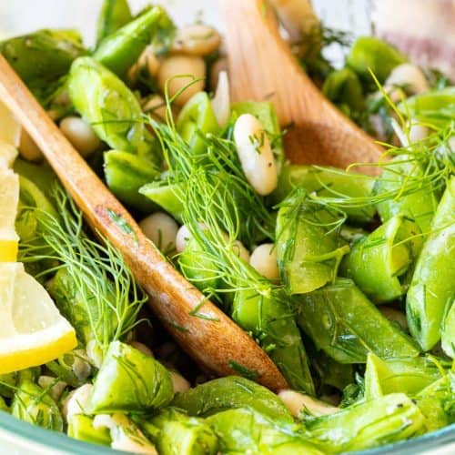 wooden spoons scooping out some of the salad in a glass bowl.