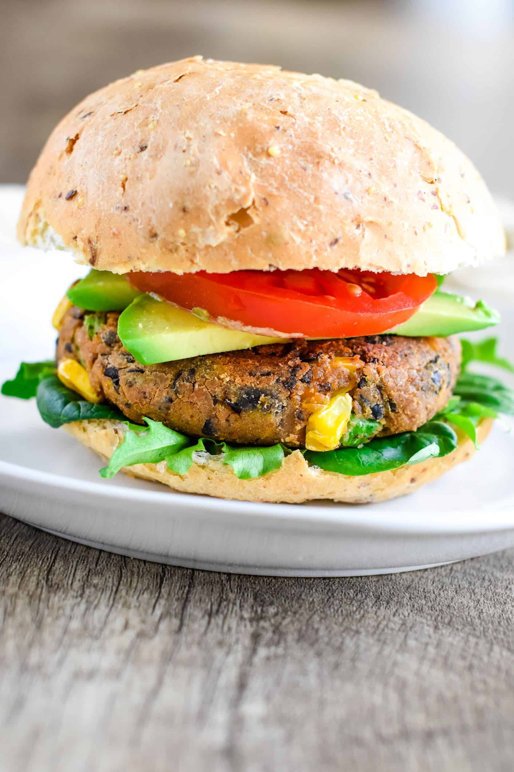 front view of sweet potato black bean burger with avocado, tomato, and bun on a white plate.