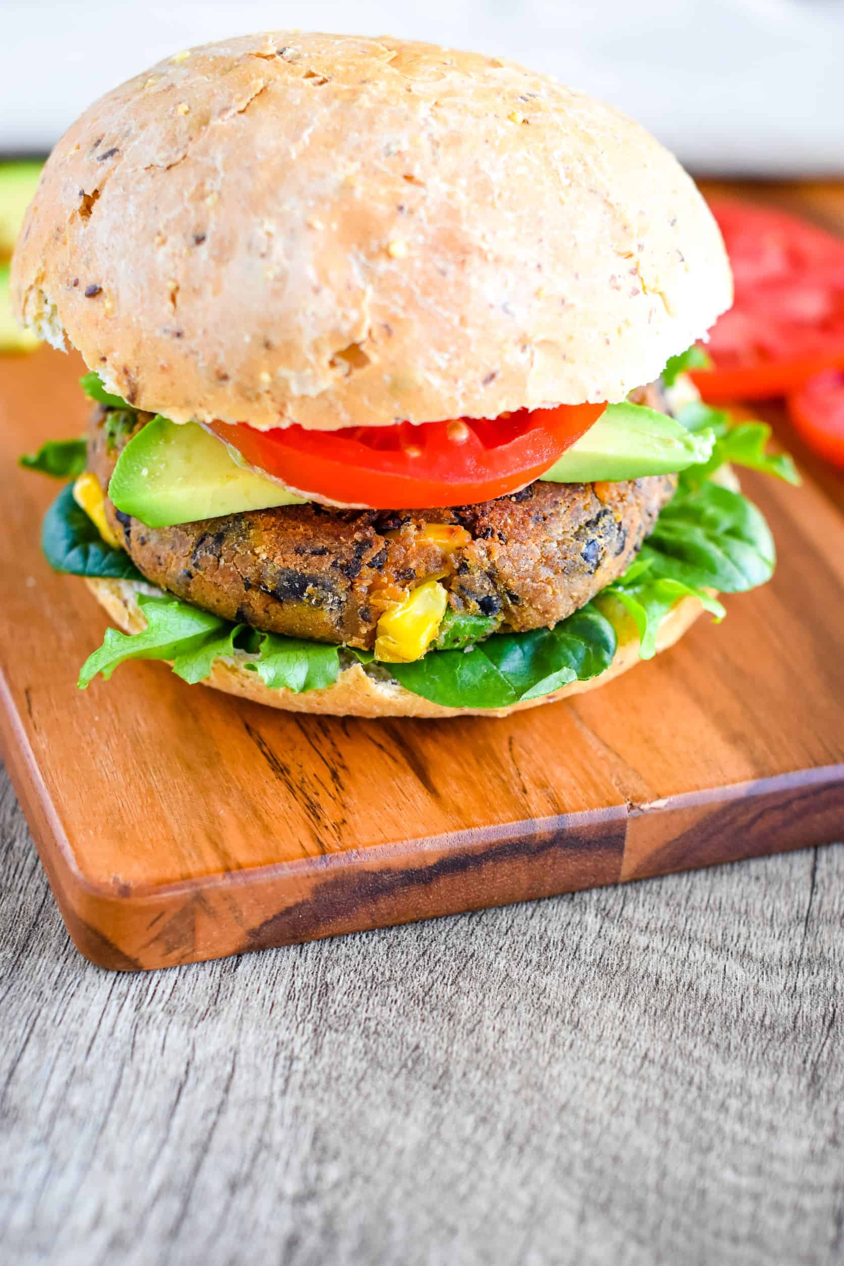 veggie burger with toppings and bun on a wooden board.
