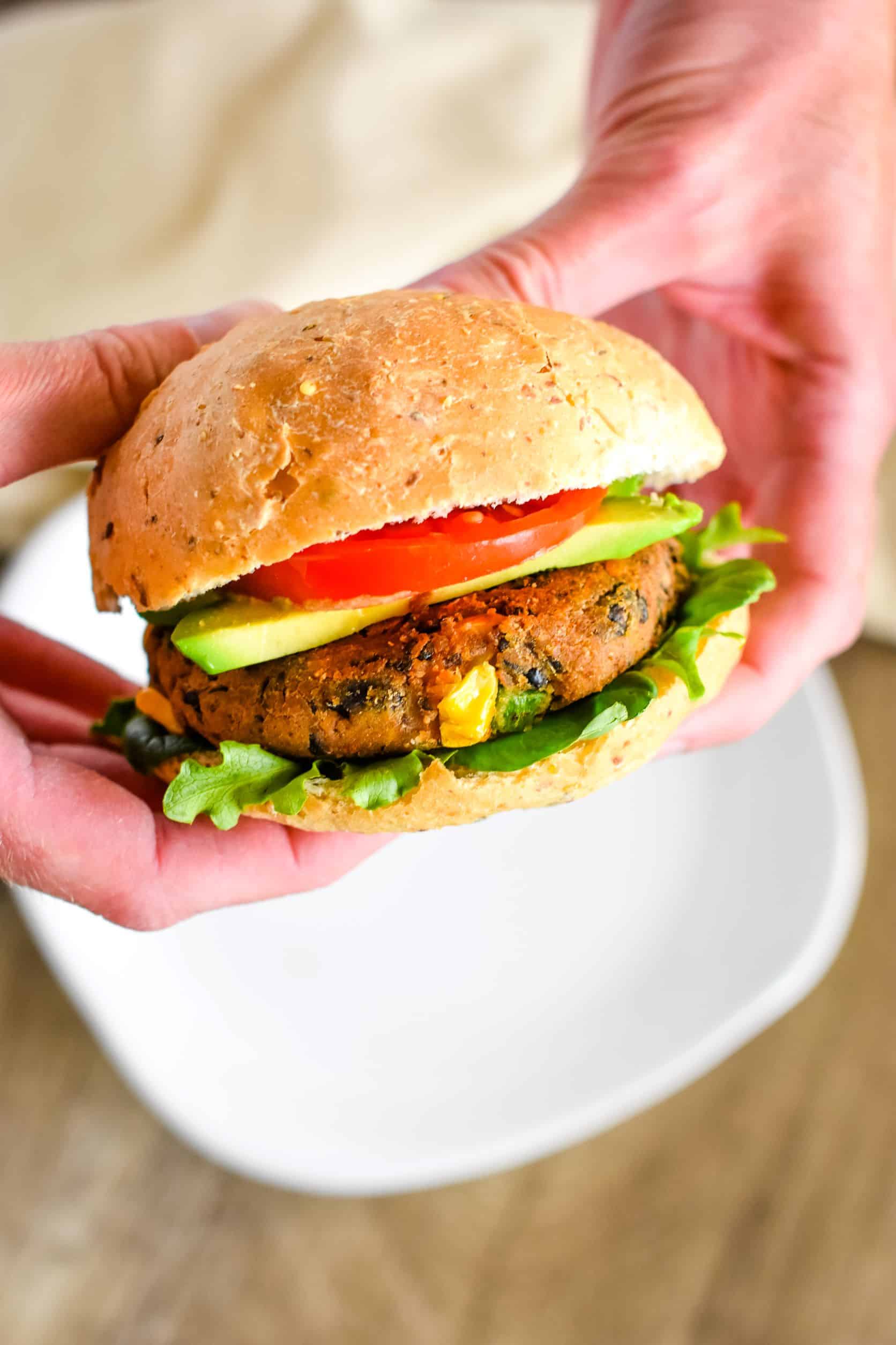 two hands holding a veggie burger up over a plate.
