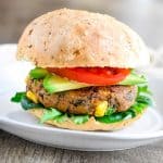 close-up of veggie burger with toppings and bun on a white plate.