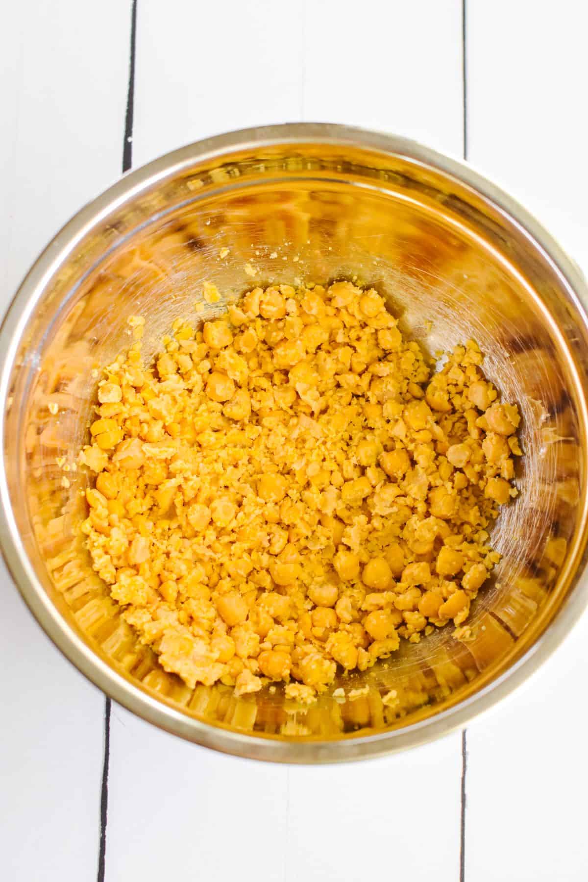 Overhead view of smashed chickpeas in a mixing bowl.